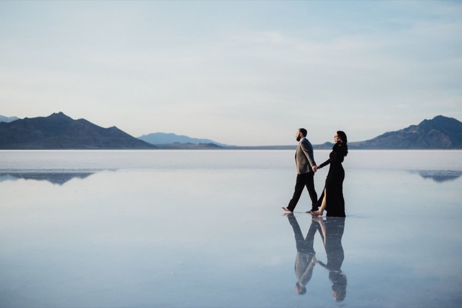 A couple walks hand in hand across the mirror of the Salt Flats