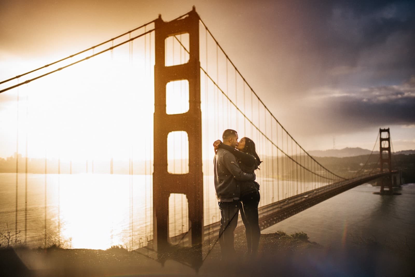 A couple kisses in front of the Golden Gate Bridge at sunset